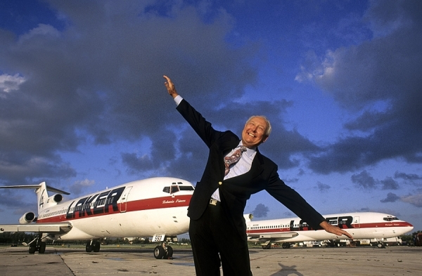 Sir Freddie Laker in a suit, arms outstretched, on the tarmac in front of Laker Airways Skytrain aircraft